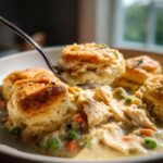A spoonful lifts a fluffy biscuit out of a bowl of creamy slow cooker chicken pot pie filling with shredded chicken and vegetables.
