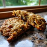 Close-up of a soft oatmeal raisin cookie broken in half, showing the chewy texture and raisins inside.