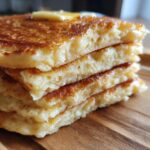 Close-up of a tall stack of four fluffy pancakes topped with melting butter and syrup.