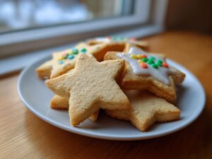 Close-up of star-shaped vegan sugar cookies, some plain and some topped with white icing and colorful sprinkles.