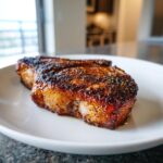 A thick, juicy air fryer pork chops cut, heavily seasoned with a dark crust, resting on a white plate.