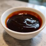 Close-up of thick, glossy homemade teriyaki sauce in a small white bowl, showing rich dark brown color.