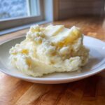 A generous serving of ultra creamy mashed potatoes with melted butter visible on top, presented on a white plate.