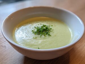 Close-up of a bowl of smooth, velvety celery soup garnished with fresh chopped green herbs.