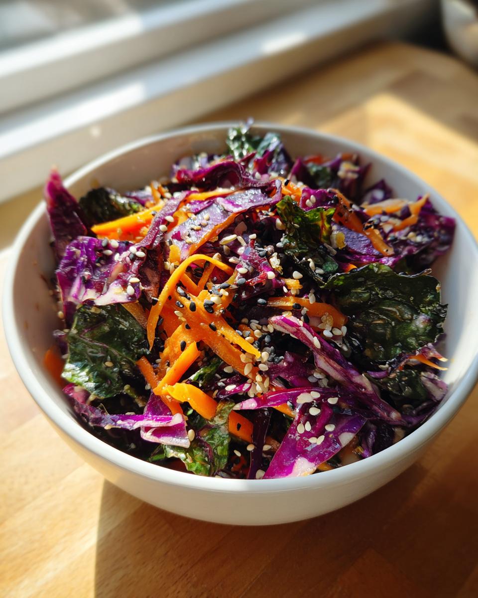 Close-up of a vibrant Asian cabbage salad featuring shredded red cabbage, carrots, and kale topped with black and white sesame seeds.