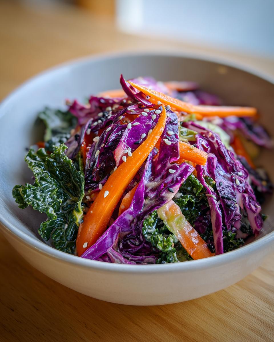 Close-up of a vibrant Asian cabbage salad featuring shredded purple cabbage, bright orange carrots, and dark green kale, topped with sesame seeds.