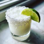 A creamy White Christmas Margarita garnished with shredded coconut rim and a fresh lime wedge.