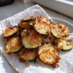 A pile of golden brown, crispy air fryer zucchini chips resting on a white paper towel.