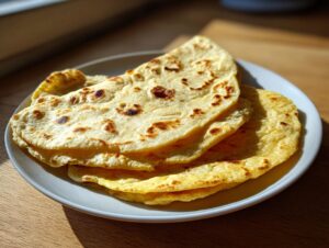 A stack of soft, freshly cooked corn tortillas with light brown char marks on a white plate.