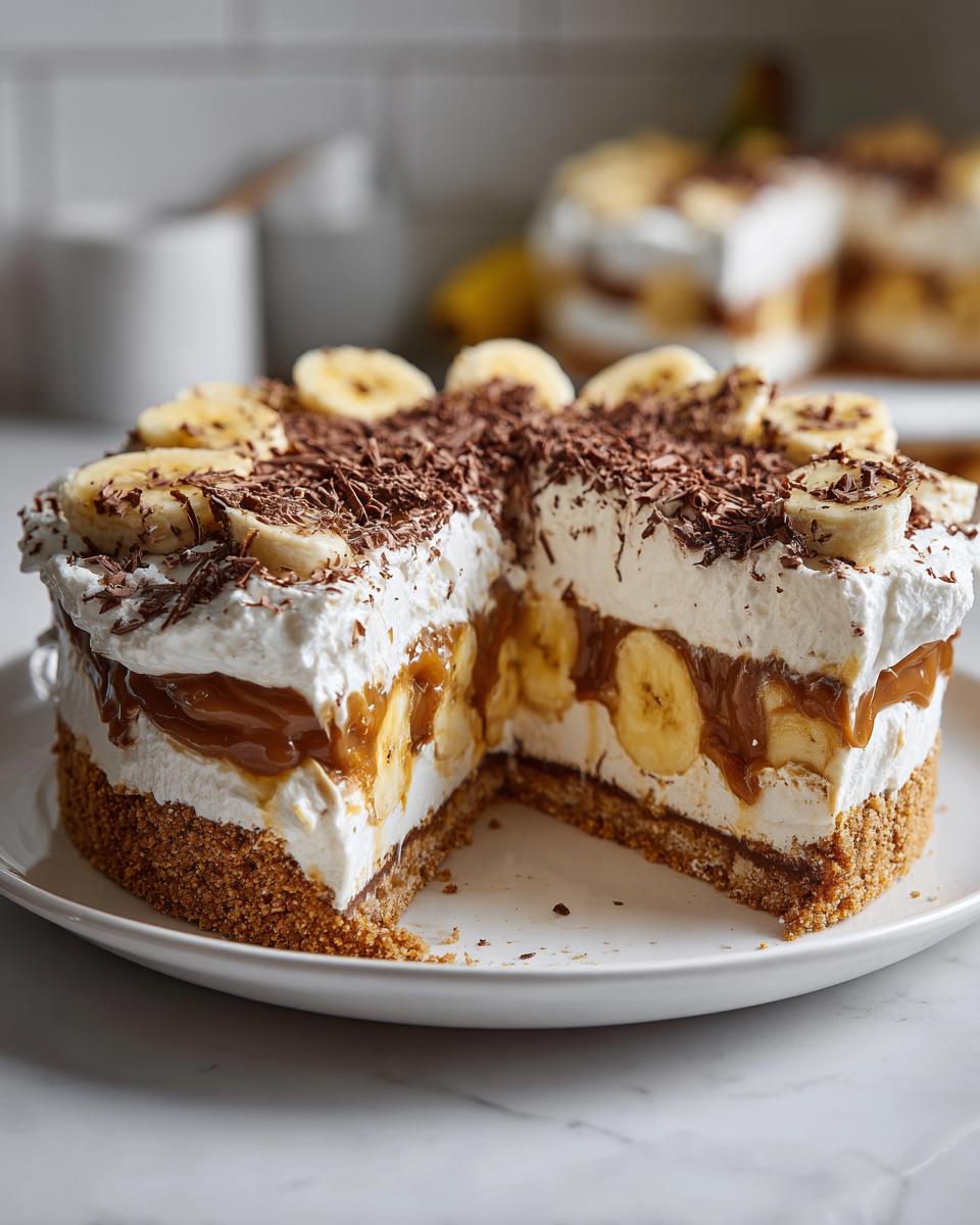 A decadent banoffee pie with a slice removed, showing layers of biscuit base, bananas, toffee, and whipped cream, topped with chocolate shavings.