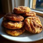 A stack of freshly baked churro cookies generously coated in sparkling cinnamon sugar, sitting on a white plate.