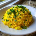 A mound of bright yellow turmeric rice topped generously with fresh chopped parsley, served on a white plate.