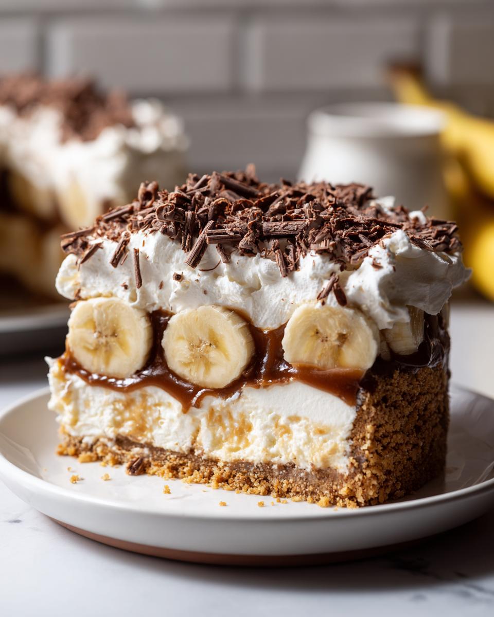 A thick slice of banoffee pie featuring a graham cracker crust, cream filling, banana slices, caramel, and chocolate shavings.