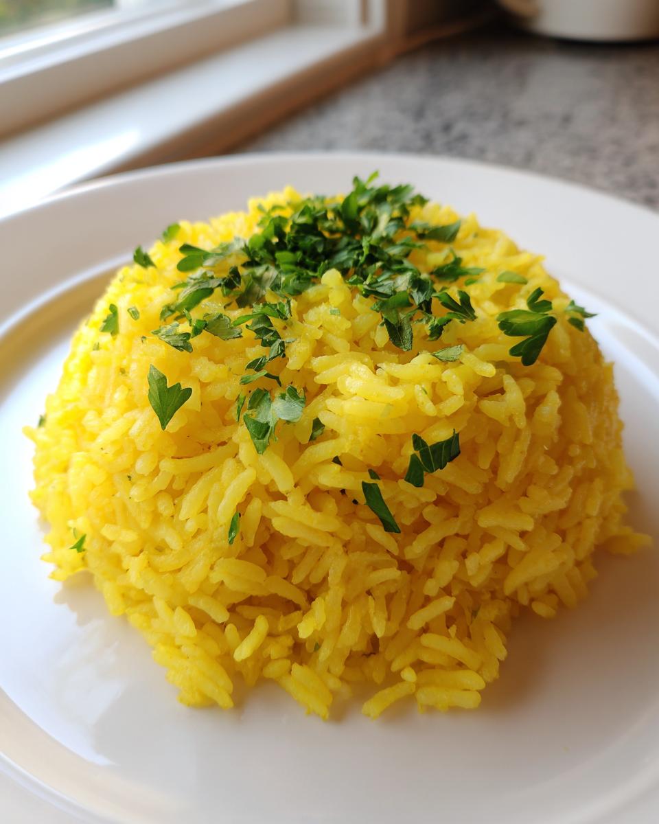 A perfectly molded serving of bright yellow turmeric rice topped with fresh chopped parsley on a white plate.