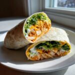 Two halves of a buffalo chicken wraps showing shredded chicken, lettuce, cheese, and ranch dressing inside a tortilla.