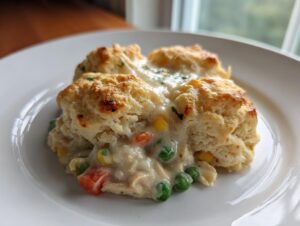 A serving of creamy chicken pot pie casserole topped with golden biscuits on a white plate.