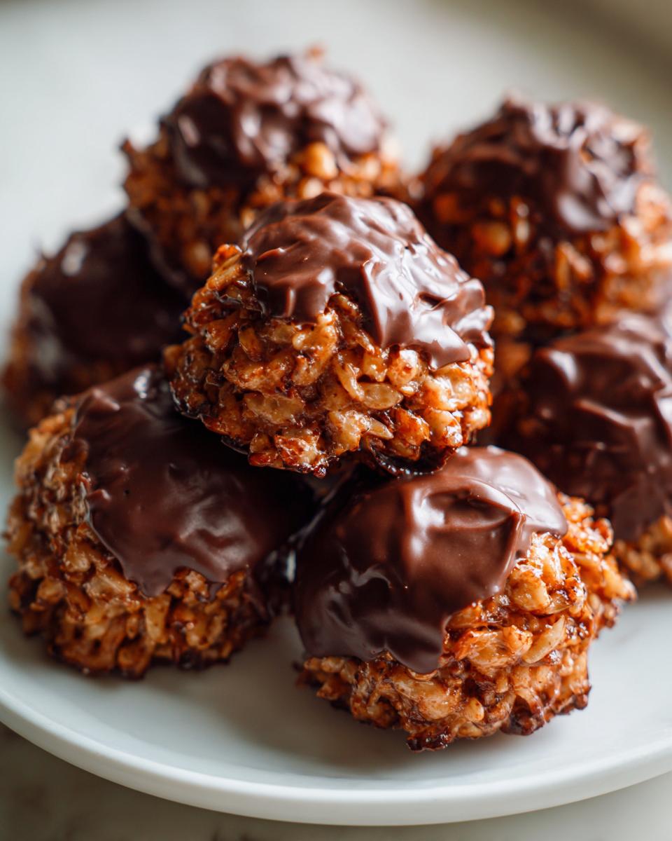 A stack of homemade chocolate rice krispie balls topped with melted dark chocolate, resting on a white plate.
