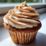 A close-up photo of a single, perfectly frosted churro cupcake dusted heavily with cinnamon sugar.