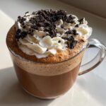 Close-up of a rich cookie butter latte topped with whipped cream and dark cookie crumbles.