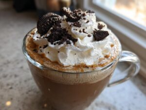 Close-up of a rich cookie butter latte topped with whipped cream and crushed chocolate cookies.