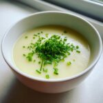 A close-up of a bowl of creamy, pale leek soup topped generously with freshly chopped green chives.