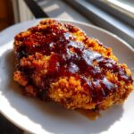 Close-up of a piece of crispy fried chicken coated in a thick, dark hot honey glaze.