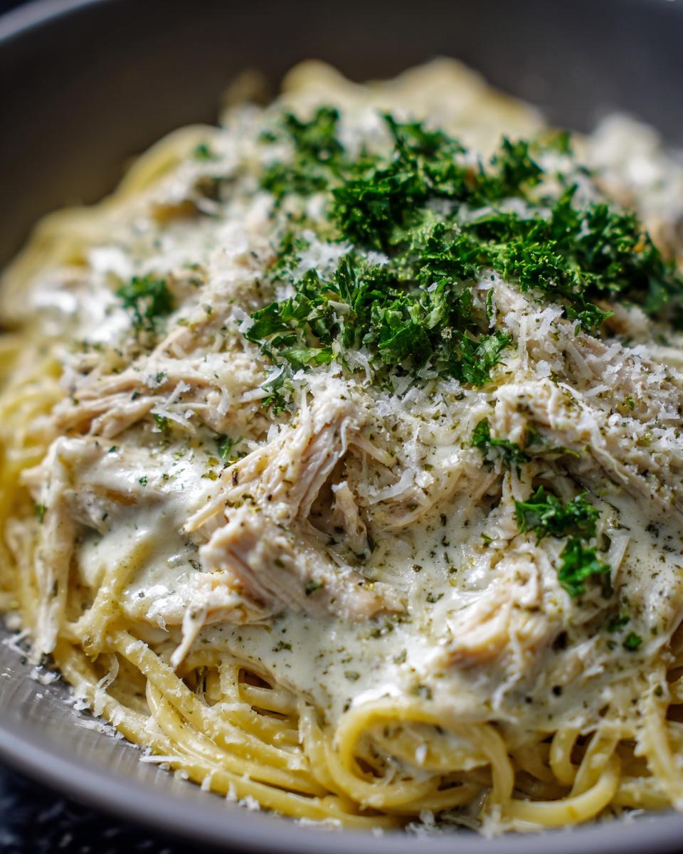 Close-up of creamy crock pot angel chicken served over spaghetti, topped with Parmesan and fresh parsley.