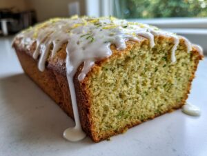 A close-up shot of a freshly baked lemon zucchini bread loaf with thick white glaze dripping down the side.