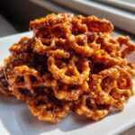 A pile of crunchy, glazed toffee pretzels coated in shiny caramel, sprinkled with salt flakes.