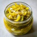 Close-up of homemade bread and butter pickle slices and onions preserved in a clear glass jar.