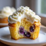 Close-up of a lemon blueberry cupcakes with a bite taken out, showing moist cake and blueberries.