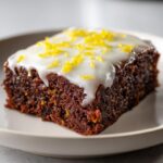 A single square of rich, dark lemon brownies topped with thick white glaze and bright yellow lemon zest.