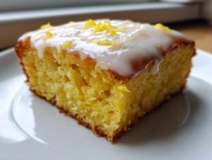 A moist, square slice of bright yellow lemon brownies topped with white glaze and lemon zest.