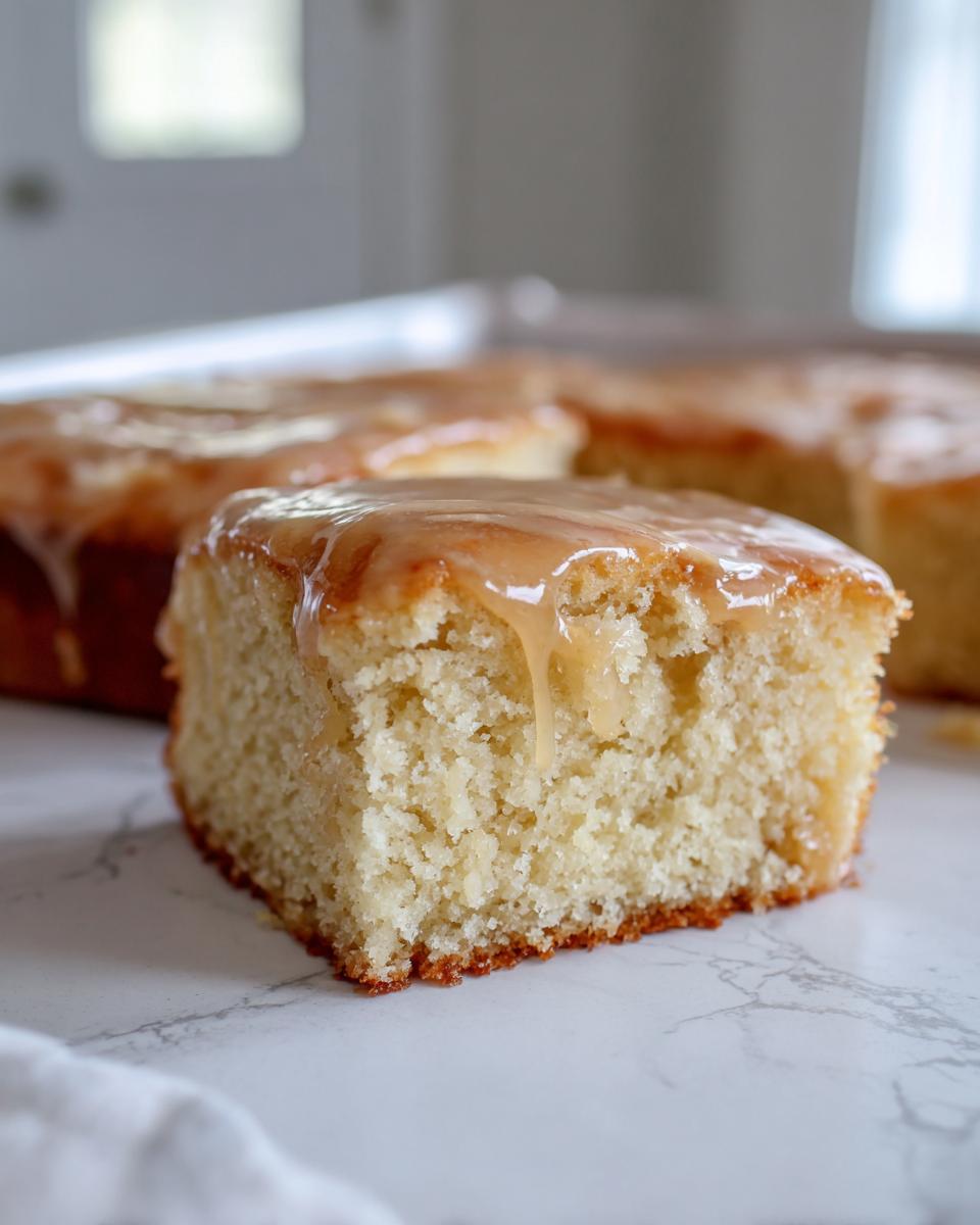 A soft, square piece of maple donut bars topped with a thick, dripping maple glaze on a white marble surface.