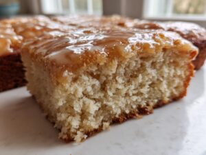 A close-up view of a soft, moist square cut from maple donut bars topped with a shiny maple glaze.