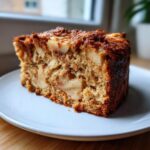A close-up of a moist slice of jewish apple cake showing chunks of baked apple throughout the crumb.