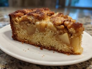 Close-up of a moist slice of jewish apple cake showing chunks of apple and a browned, sugary top.