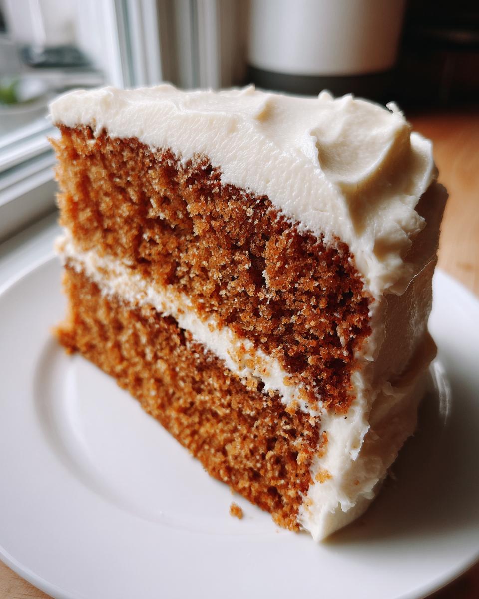 Close-up of a moist slice of spice cake layered with thick cream cheese frosting on a white plate.
