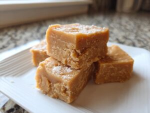 Close-up of four creamy squares of peanut butter fudge recipe dusted lightly with powdered sugar on a white plate.