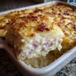A serving of creamy scalloped potatoes and ham being lifted from a baking dish, showing layers and a golden, crispy top.