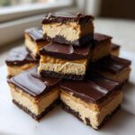 A stack of rich, layered buckeye fudge bars featuring a dark chocolate base, peanut butter filling, and chocolate topping.