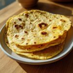 A stack of warm, freshly cooked yellow corn tortillas with light brown char marks on a light plate.