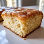 A close-up, tasty shot of a soft, square slice of maple donut bars topped with a shiny maple glaze.