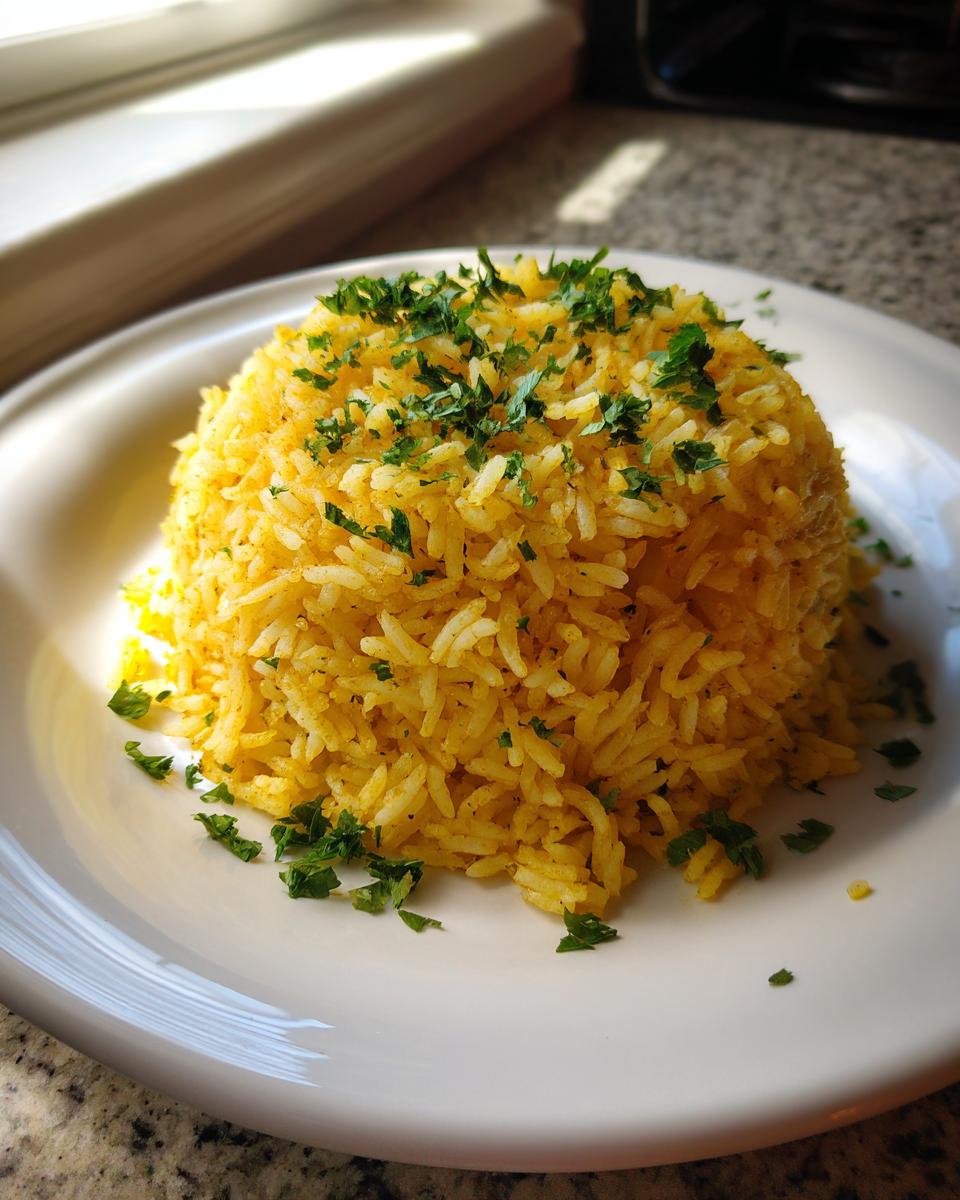 A mound of bright yellow turmeric rice garnished with fresh chopped parsley, served on a white plate.