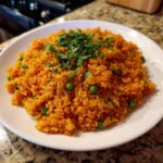 A close-up of vibrant orange Mexican rice mixed with green peas, topped with fresh cilantro.