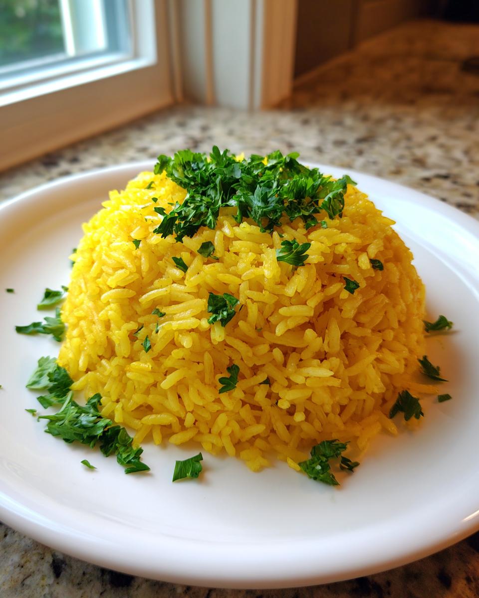A perfectly molded mound of bright yellow turmeric rice garnished generously with fresh chopped parsley on a white plate.