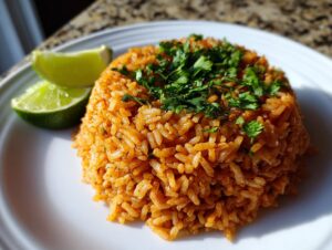 A mound of vibrant orange Spanish rice garnished with fresh cilantro and served with two lime wedges on a white plate.