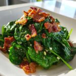 Close-up of a warm spinach salad topped generously with crispy crumbled bacon pieces.