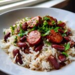 Close-up of a bowl of flavorful beans and rice topped with sliced smoked sausage and fresh parsley.