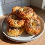 A stack of golden brown greek yogurt bagels topped with black sesame seeds resting on a light gray plate.